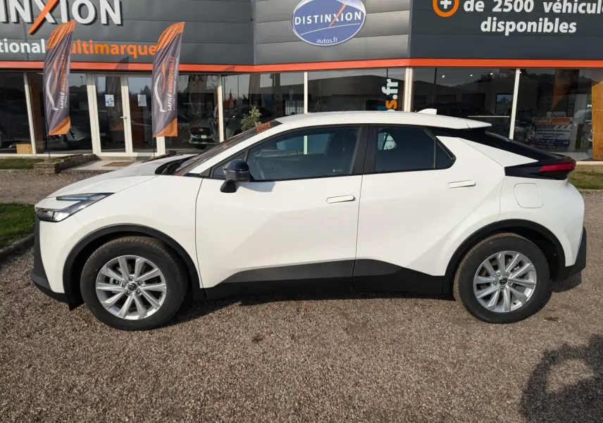 Vue de profil côté gauche du Toyota C-HR 1.8 Hybrid blanc avec jantes alliage 17 pouces sur parking extérieur.