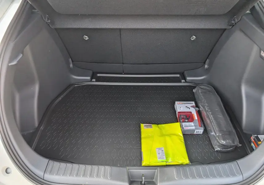 Coffre ouvert du Toyota C-HR blanc 2024, vue plongeante montrant tapis de coffre et kit de sécurité.