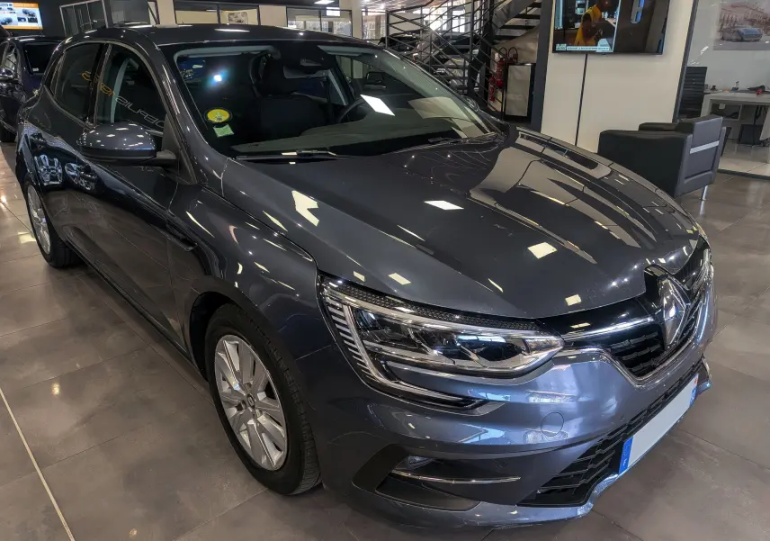 Renault Mégane IV Berline Blue dCi 115 en gris titanium, vue 3/4 avant droit dans un showroom intérieur.
