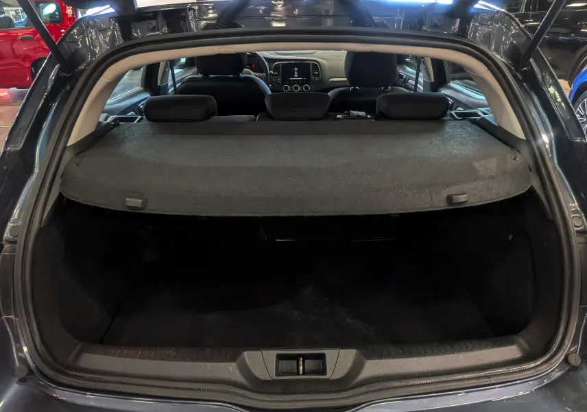 Coffre ouvert vu de l'arrière d'une Renault Mégane IV Berline gris Titanium, avec tablette cache-bagages en place.