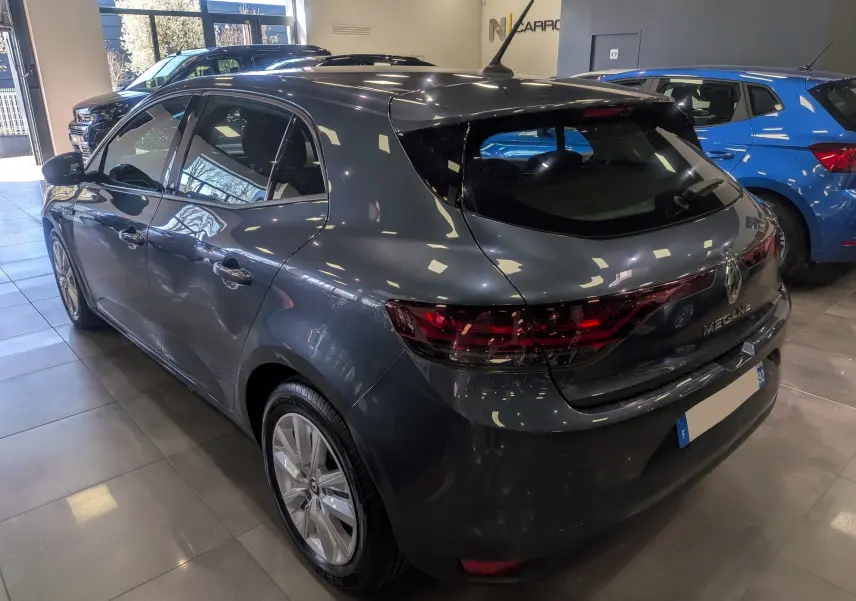 Vue 3/4 arrière droite d'une Renault Mégane IV berline gris Titanium, avec feux arrière LED et jantes alliage en showroom.