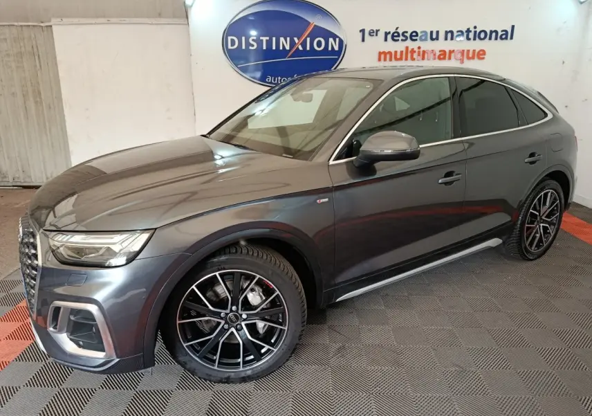 Audi Q5 gris clair 2023 en 3/4 avant droit, avec jantes noires et détails chromés, dans un showroom intérieur.