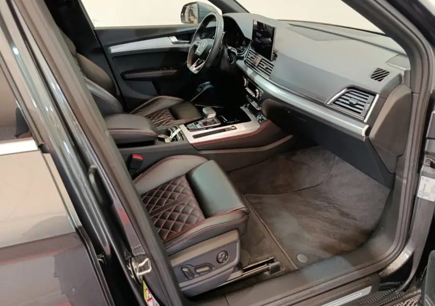 Vue intérieure côté conducteur de l'Audi Q5 2023 hybride rechargeable, sièges cuir noir avec surpiqûres rouges et tableau de bord moderne.