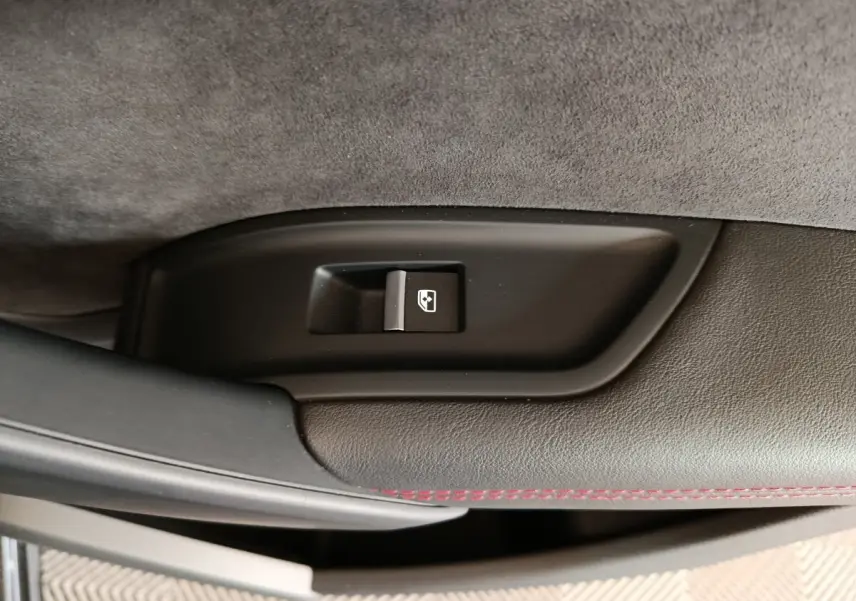Détail du bouton d'ouverture du coffre sur la garniture intérieure noire avec surpiqûres rouges d'un Audi Q5 gris clair 2023.