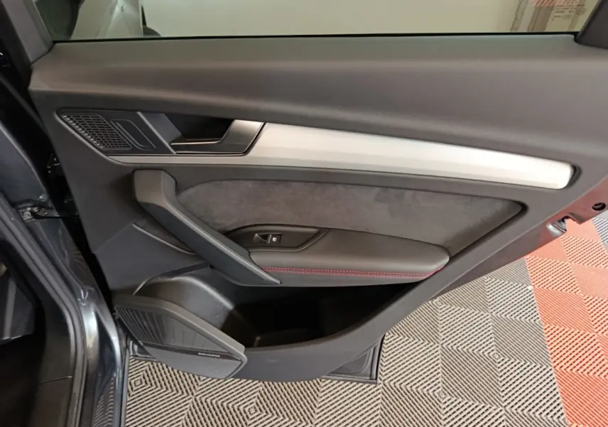 Vue intérieure du panneau de porte côté gauche de l’Audi Q5 2023 gris clair, avec insert en aluminium et haut-parleur Bang & Olufsen.