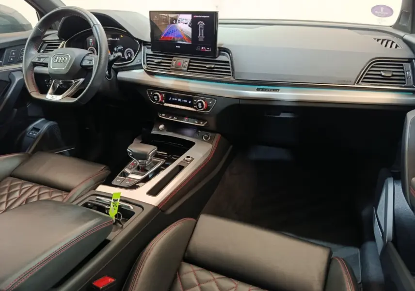 Vue intérieure de l'Audi Q5 2023 hybride rechargeable, montrant le tableau de bord, volant et console centrale en cuir noir avec surpiqûres rouges.