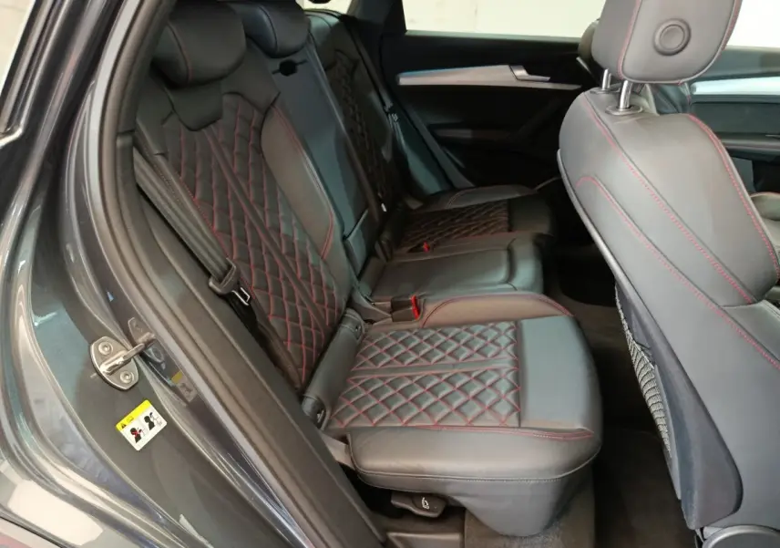 Vue intérieure côté gauche des sièges arrière en cuir noir avec surpiqûres rouges de l'Audi Q5 gris clair 2023 hybride rechargeable.