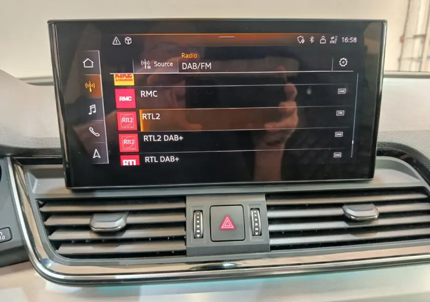 Écran central tactile de l'Audi Q5 2023 affichant les options radio DAB/FM, avec commandes d'aération en dessous.