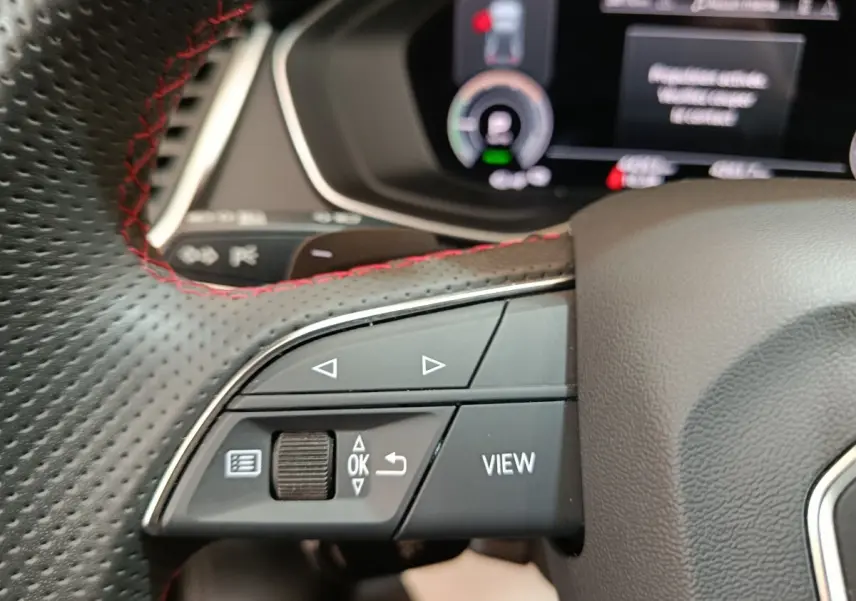 Gros plan sur les commandes gauche du volant perforé avec surpiqûres rouges de l'Audi Q5 hybride rechargeable 2023.