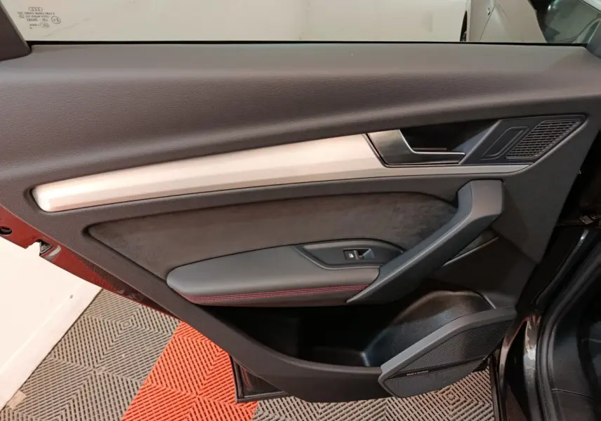 Intérieur de la porte côté gauche de l’Audi Q5 2023 gris clair, avec garniture noire et surpiqûres rouges.