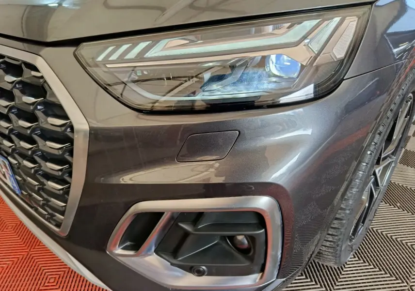 Gros plan sur l'avant droit gris clair de l'Audi Q5 2023 hybride rechargeable, mettant en valeur le phare et la calandre.