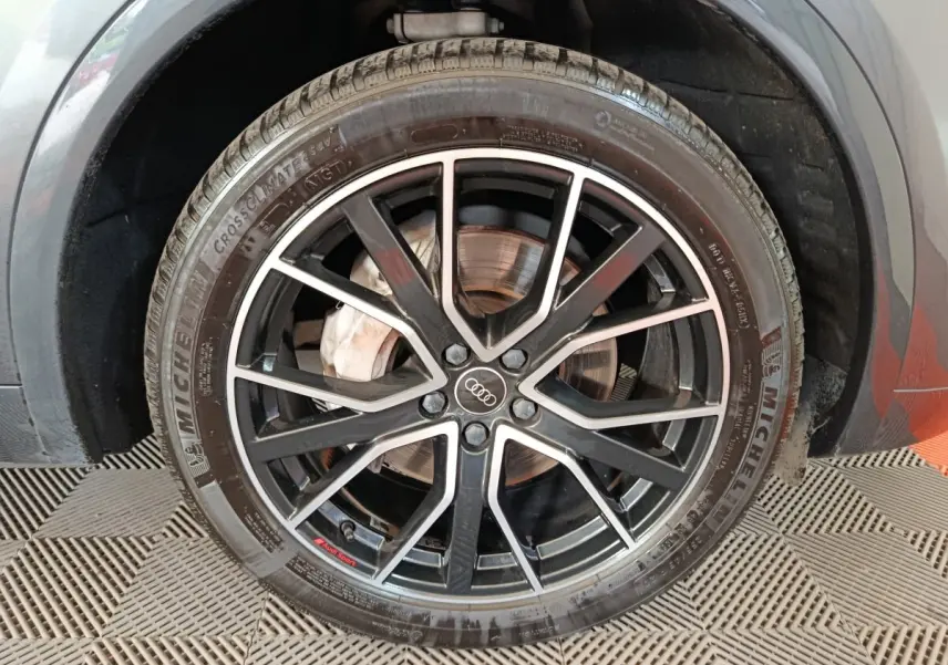 Gros plan sur la roue avant droite d’un Audi Q5 gris clair 2023, jante noire à branches fines avec logo Audi au centre.