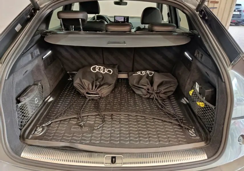Coffre ouvert d’un Audi Q5 gris clair 2023, vue arrière montrant tapis de protection et sacs noirs avec logo Audi.
