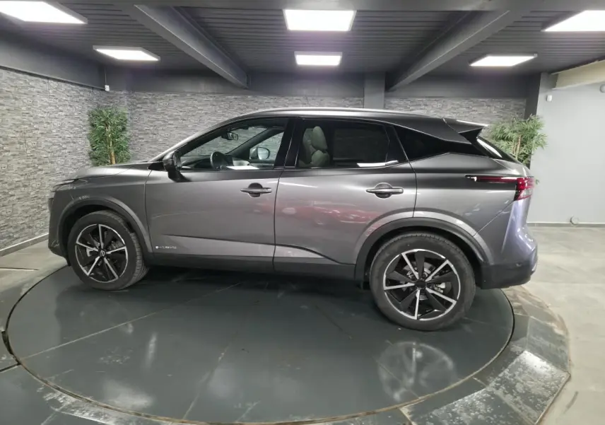 Vue de profil côté gauche d'un Nissan Qashqai 1.5 e-Power gris métallisé avec toit noir et jantes alliage 19 pouces.