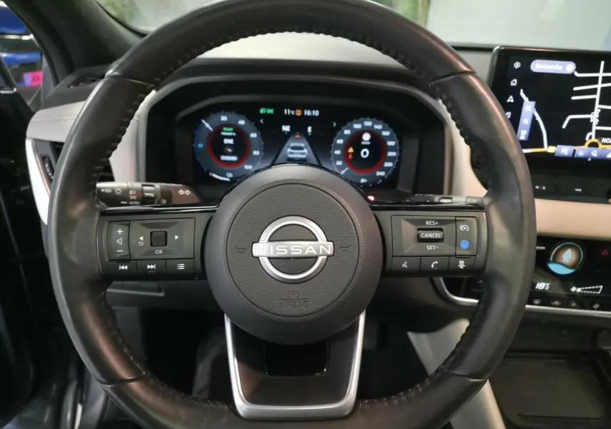 Vue intérieure centrée sur le volant cuir noir et le tableau de bord avec écran tactile du Nissan Qashqai 2024 gris.