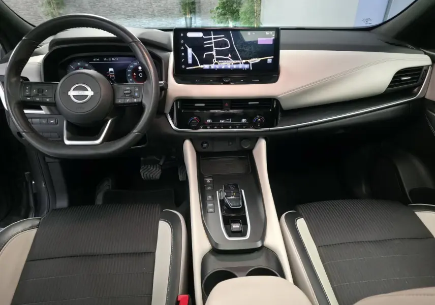 Intérieur du Nissan Qashqai 1.5 e-Power 2024, vue frontale du tableau de bord avec écran tactile et sellerie bicolore noire et beige.