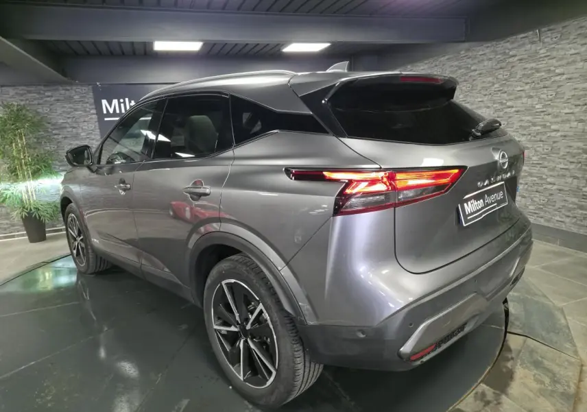Vue 3/4 arrière droit d'un Nissan Qashqai gris métallisé avec toit noir et feux arrière LED allumés.