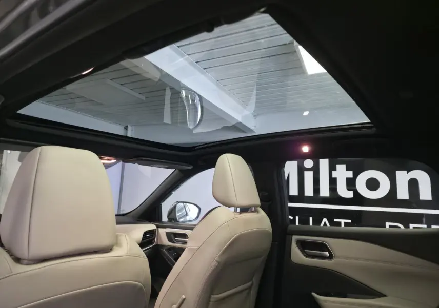 Vue intérieure arrière droite du Nissan Qashqai gris 2024 avec toit panoramique en verre et sièges clairs.