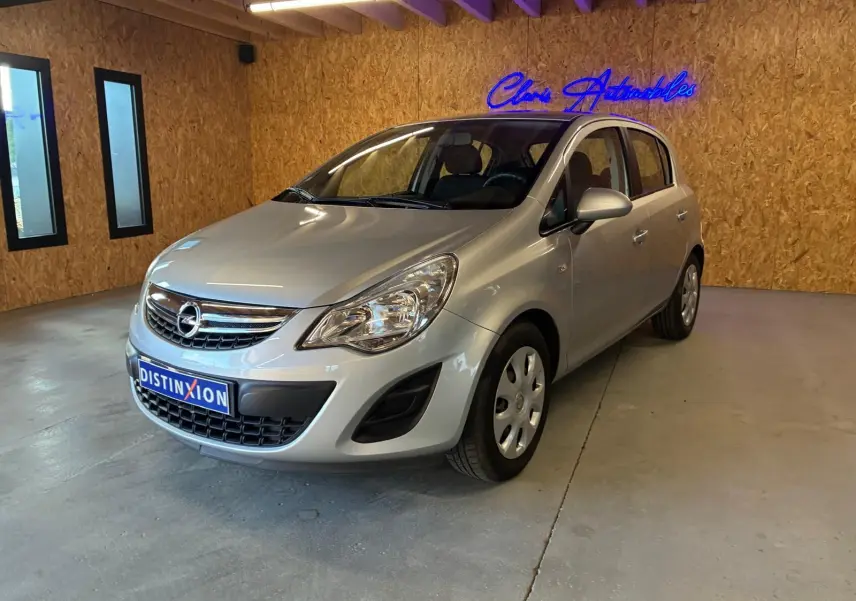 Opel Corsa gris clair vue 3/4 avant droit dans un showroom avec mur en bois et enseigne lumineuse bleue.