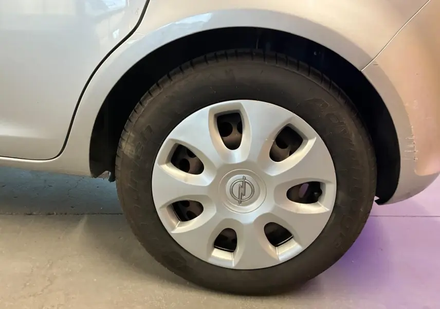 Gros plan sur la roue avant droite grise claire d'une Opel Corsa 1.2i 85 Edition de 2012 avec enjoliveur Opel.