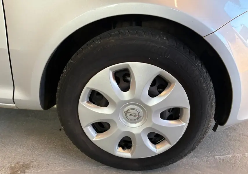 Gros plan sur la roue avant gauche d’une Opel Corsa gris clair, avec enjoliveur argenté et logo Opel au centre.