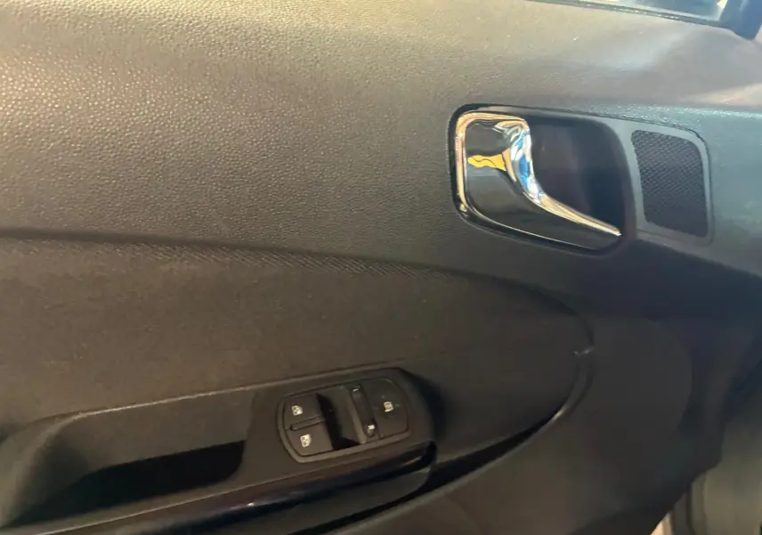 Gros plan sur la poignée intérieure et les commandes de lève-vitres côté gauche d’une Opel Corsa gris clair 2012.