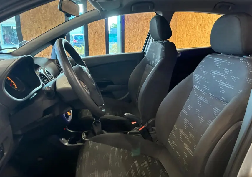 Vue intérieure côté conducteur de l’Opel Corsa gris clair 2012, sièges tissu noir avec motifs et volant multifonction.