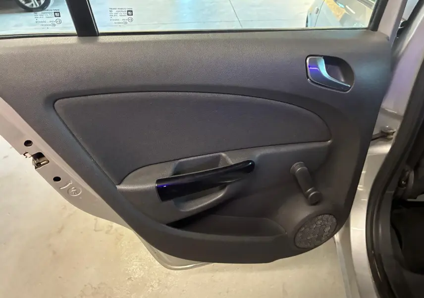 Vue intérieure de la porte arrière gauche grise claire de l'Opel Corsa 2012 avec poignée noire et manivelle de vitre.