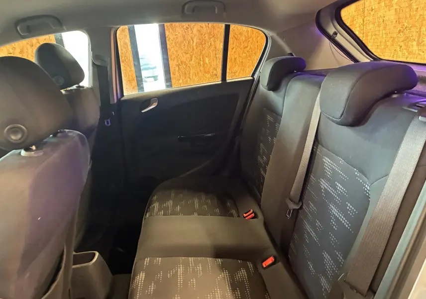 Vue intérieure arrière côté droit de l’Opel Corsa gris clair 2012, sièges tissu noir avec motifs et ceintures visibles.