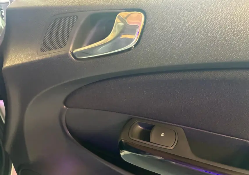 Gros plan sur la poignée intérieure chromée et le bouton de verrouillage sur la porte côté conducteur d’une Opel Corsa gris clair de 2012.