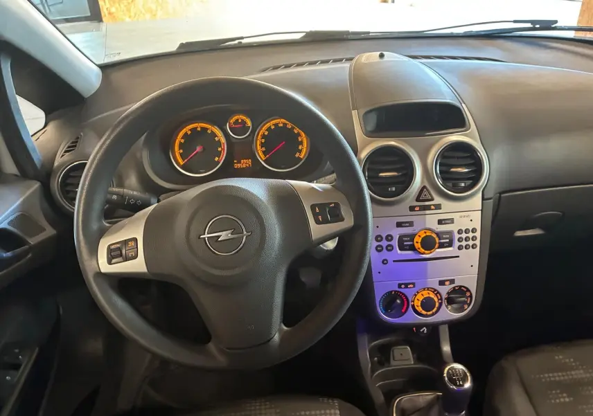 Intérieur noir de l’Opel Corsa 2012, vue du poste de conduite avec volant, tableau de bord et console centrale éclairés.