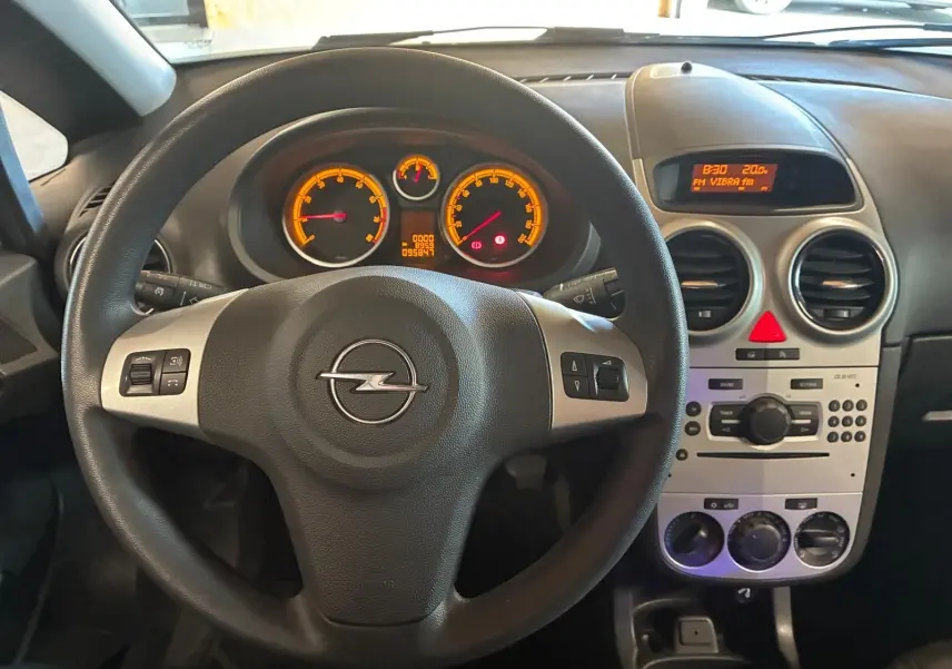 Vue intérieure centrée sur le volant noir d’une Opel Corsa 2012 avec tableau de bord et console centrale gris clair.
