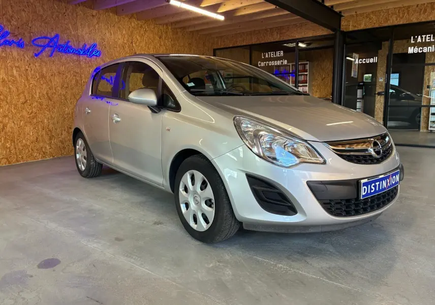 Opel Corsa gris clair 2012 vue 3/4 avant droit, compacte cinq portes avec jantes acier et calandre chromée.