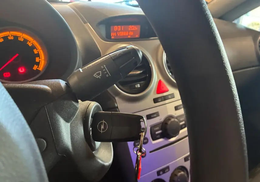 Vue intérieure centrée sur le volant et le tableau de bord d'une Opel Corsa 2012 avec clé insérée et affichage digital orange.