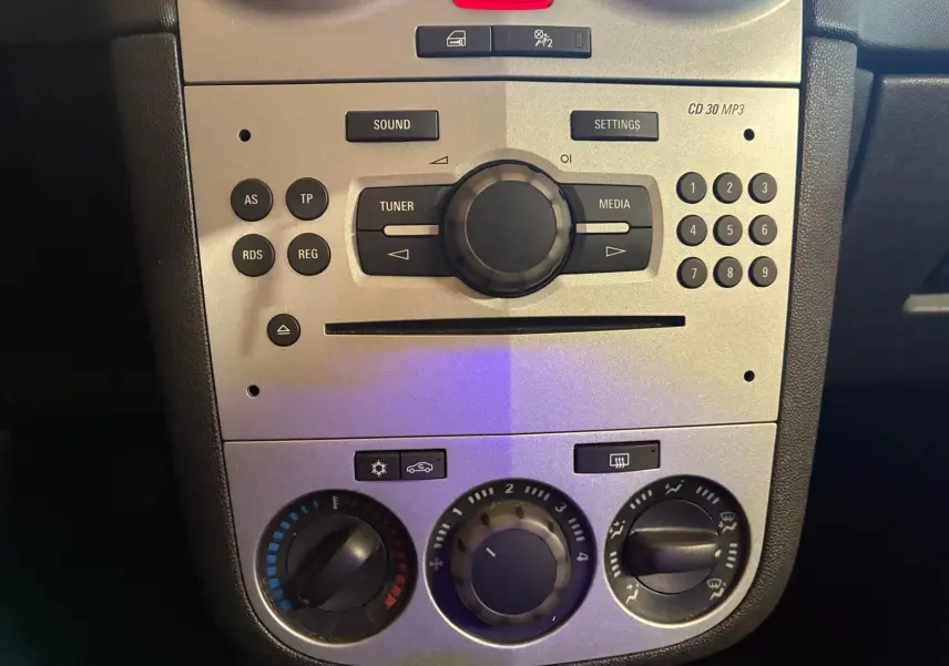 Vue rapprochée du tableau de bord gris clair de l’Opel Corsa 2012 avec commandes radio et climatisation manuelle.