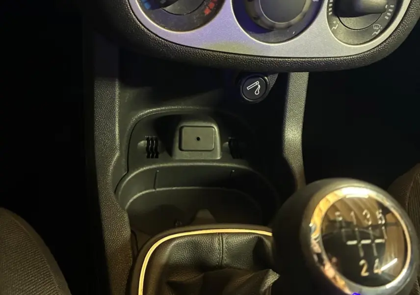 Gros plan sur la console centrale d'une Opel Corsa gris clair 2012, avec levier de vitesse manuel et commandes de climatisation.