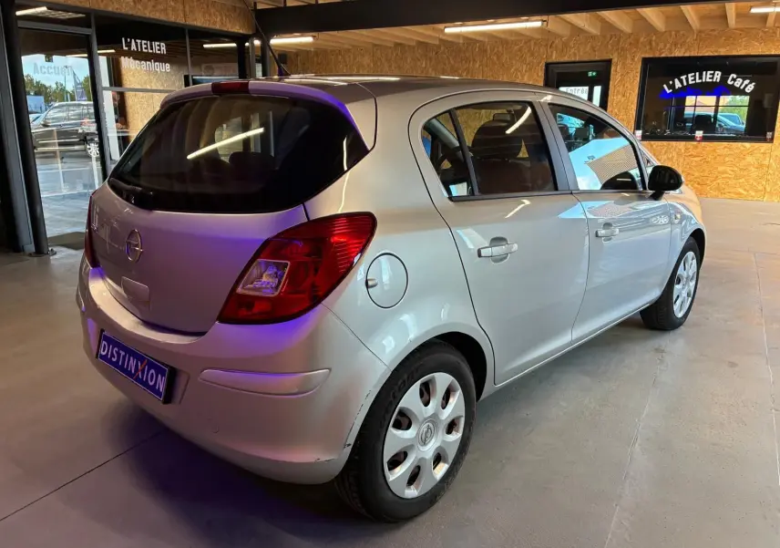 Opel Corsa gris clair vue 3/4 arrière droit dans un garage avec cinq portes et jantes acier.
