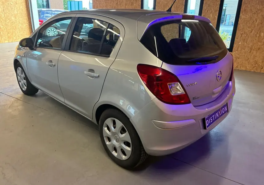 Opel Corsa gris clair vue 3/4 arrière droit, compacte 5 portes avec feux arrière rouges et jantes acier.