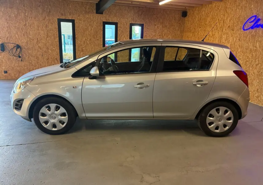 Vue latérale droite d'une Opel Corsa gris clair 5 portes de 2012, avec jantes acier et intérieur visible noir.