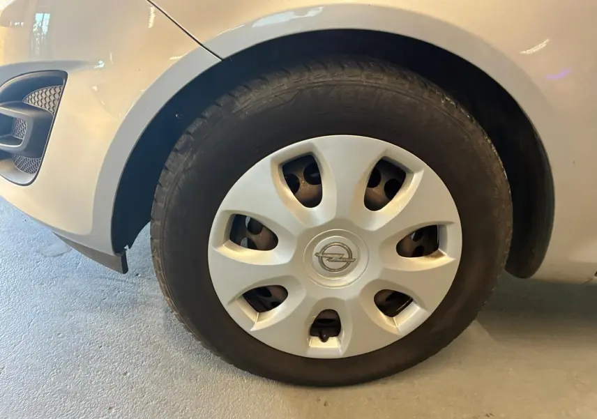 Gros plan sur la roue avant gauche grise claire d’une Opel Corsa 1.2i 85 Edition avec enjoliveur et logo Opel visible.