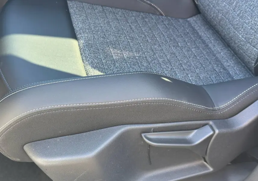 Gros plan sur l'assise en tissu gris et cuir noir avec surpiqûres blanches d'un siège avant Peugeot 5008 Hybrid 2025.