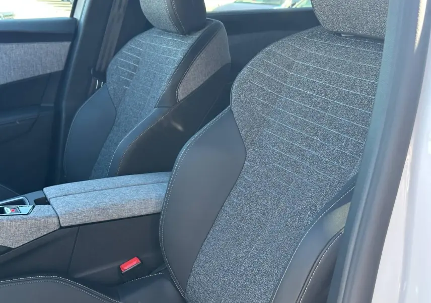 Gros plan sur les sièges avant en tissu gris et cuir noir du Peugeot 5008 Hybrid blanc, avec accoudoir central.