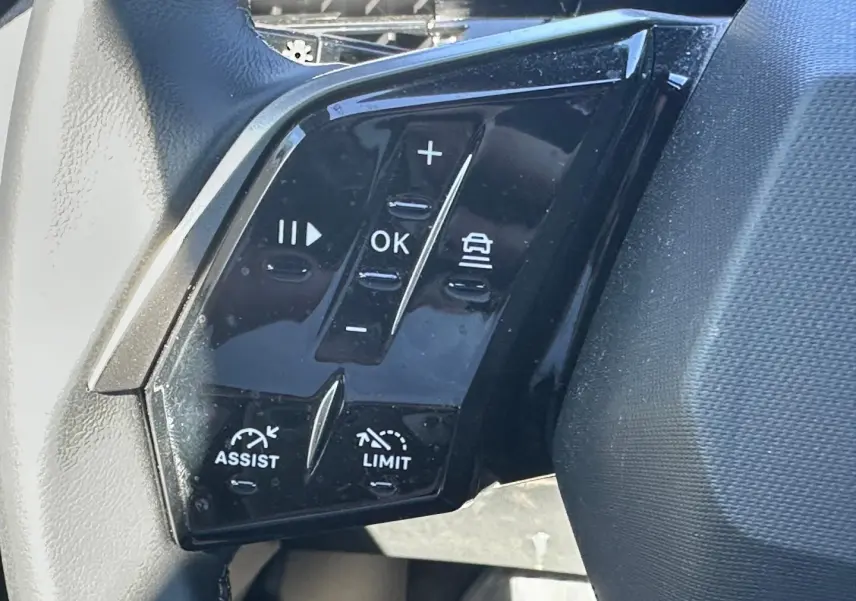 Gros plan sur les commandes multifonctions noires du volant cuir du Peugeot 5008 Hybrid blanc Okénite.