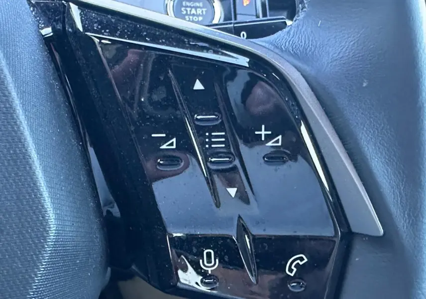 Gros plan sur les commandes noires du volant multifonction du Peugeot 5008 Hybrid blanc, avec bouton micro et téléphone.
