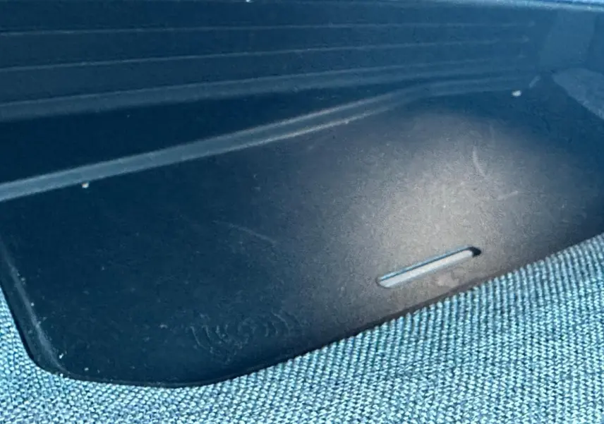 Gros plan sur le tapis de recharge sans fil noir dans l’habitacle du Peugeot 5008 Hybrid blanc Okénite.