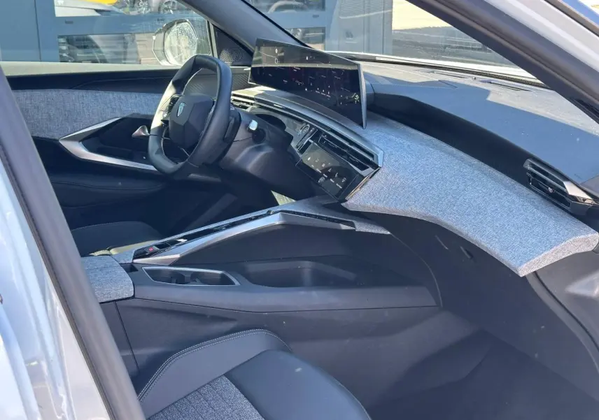 Vue intérieure côté conducteur du Peugeot 5008 Hybrid 2025, tableau de bord avec écran incurvé et tissu gris clair.