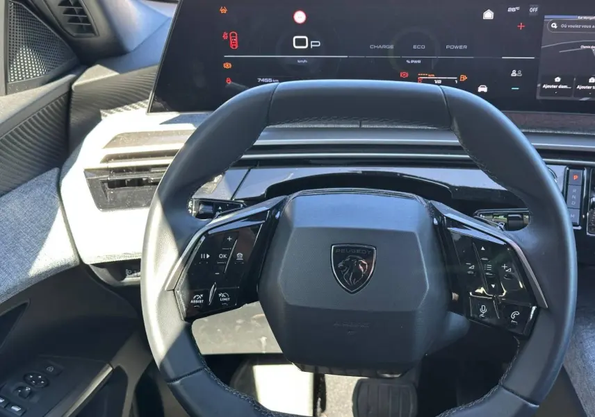 Vue rapprochée du volant cuir multifonction noir du Peugeot 5008 Hybrid 2025 avec tableau de bord numérique en arrière-plan.