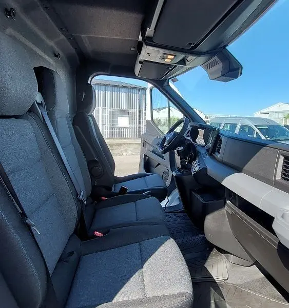 Vue intérieure côté conducteur du Nissan Interstar Fourgon 2025, sièges gris et tableau de bord moderne sous lumière naturelle.