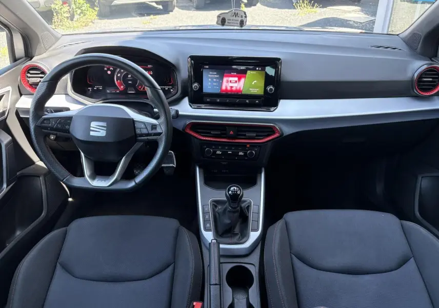 Vue intérieure avant du tableau de bord et volant cuir multifonction de la SEAT Arona 2024 avec inserts rouges et écran tactile.