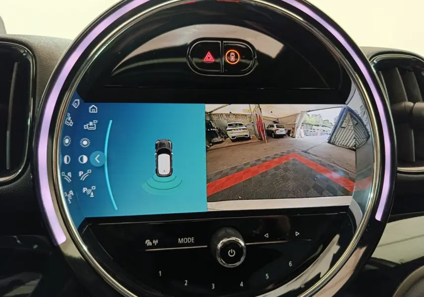Gros plan sur l'écran tactile circulaire du tableau de bord du MINI Countryman blanc, affichant la caméra de recul et l'aide au stationnement.